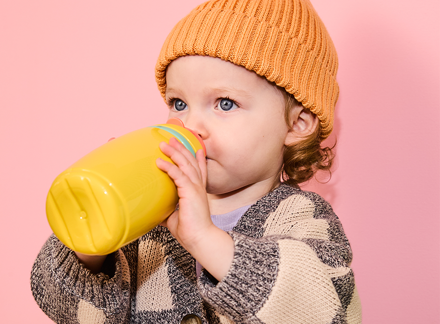 Toddler in orange hat drinking from yellow bottle
