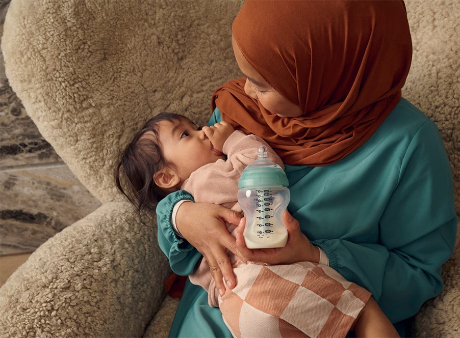 a mum holding her baby and a tommee tippee bottle