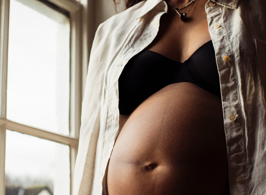 a pregnant mum sitting with her toddler on her knee who's holding her bump
