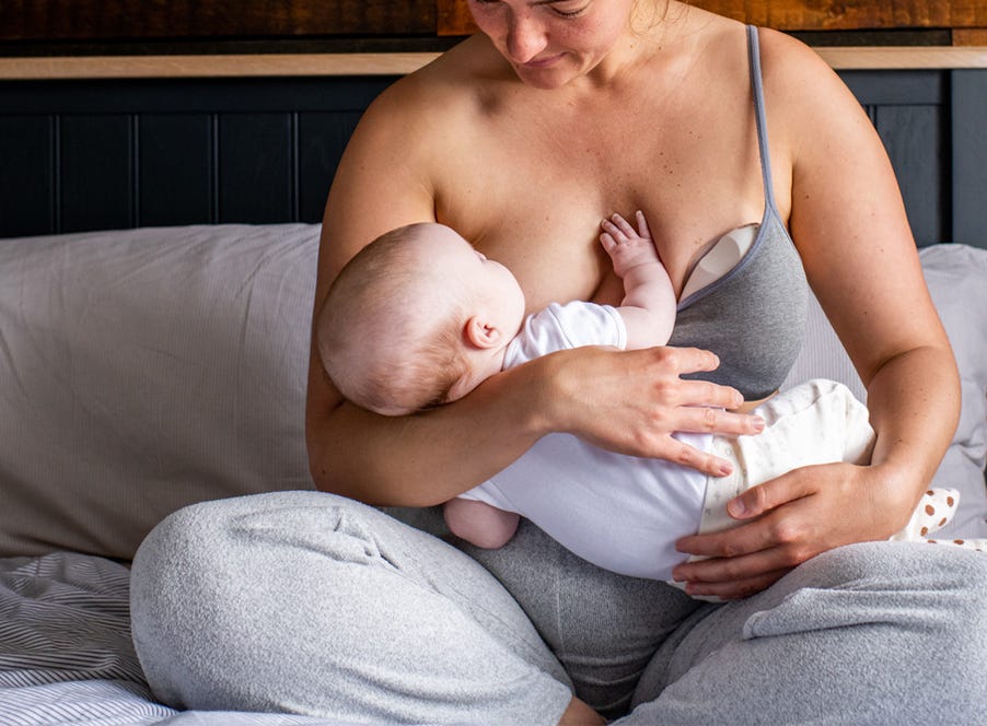 a mom breastfeeding her baby while using a wearable tommee tippee breast pump