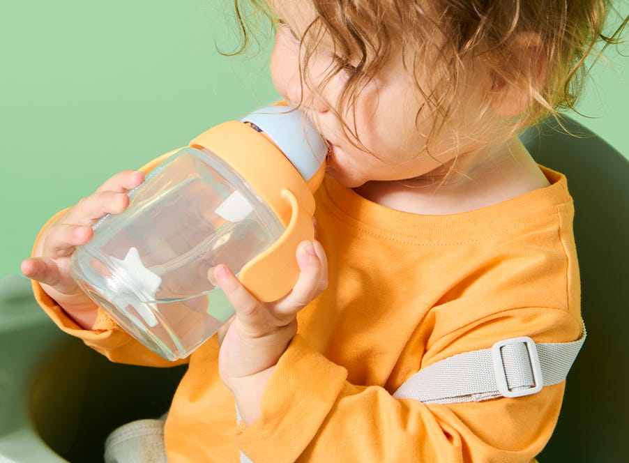 A toddler drinking from a Tommee Tippee straw cup.