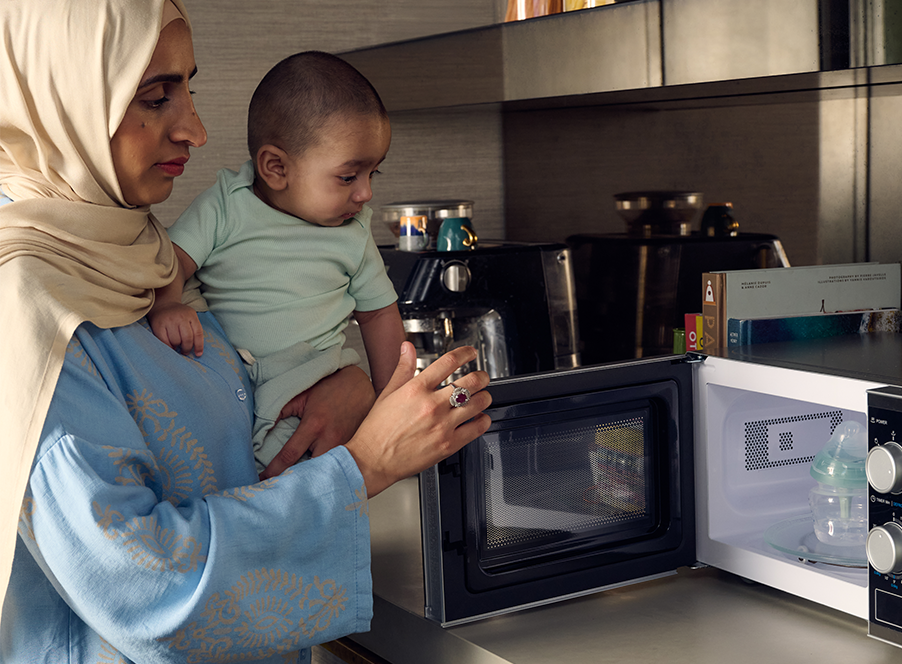mum holding baby sterilising bottle in microwave