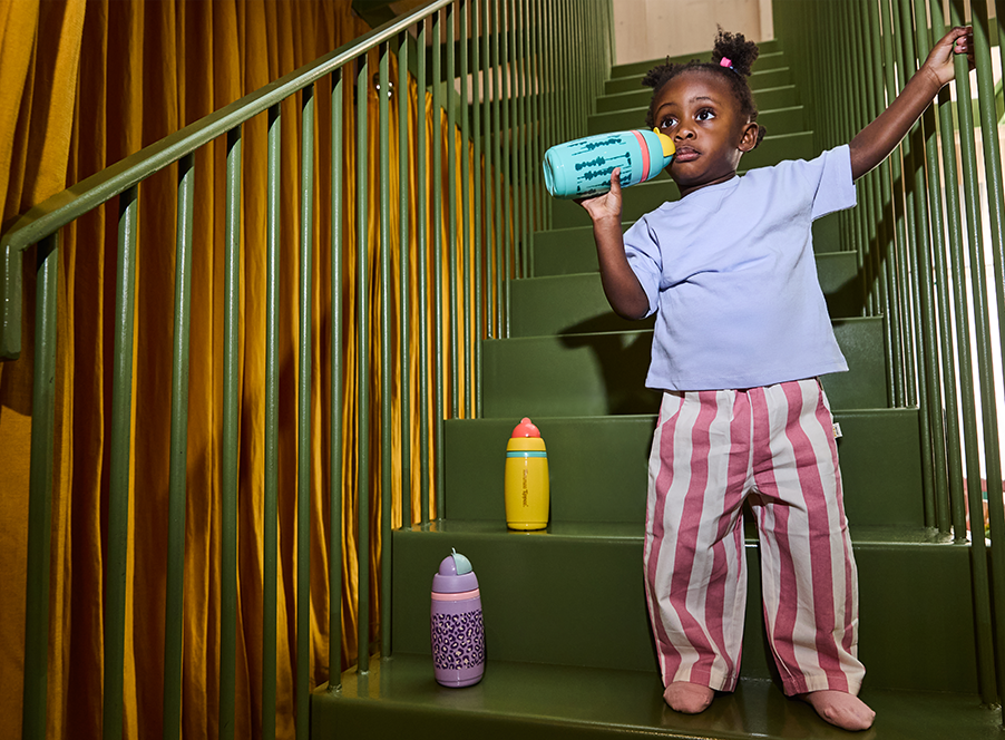 toddler standing on stairs drinking with cups