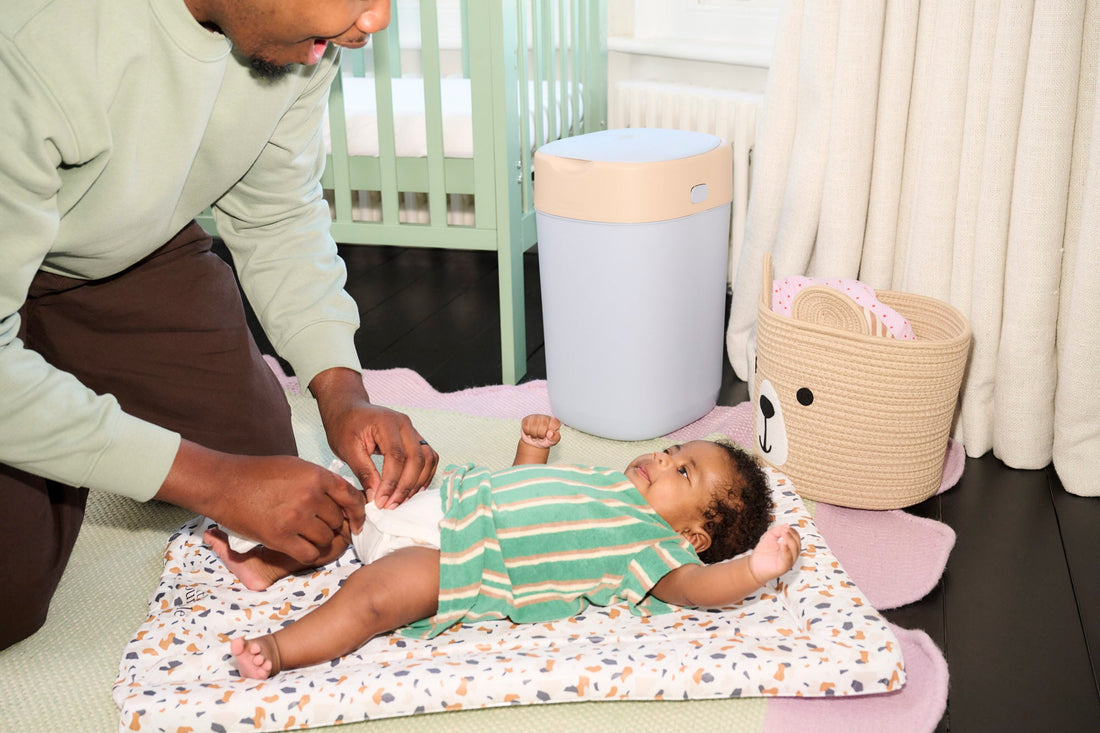 Man changing baby's nappy next to blue nappy bin