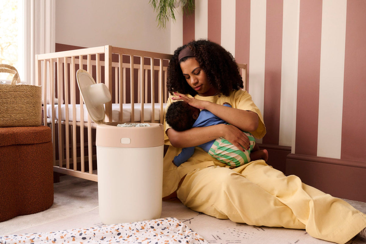 mum holding baby in nursery next to nappy bin
