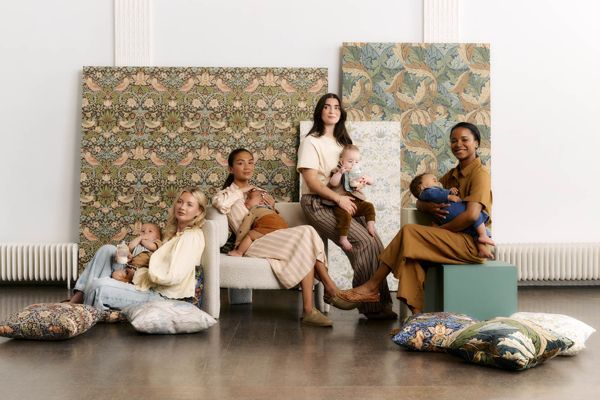 Four mums sitting on chairs and floor with babies in big room with patterned backdrops behind them