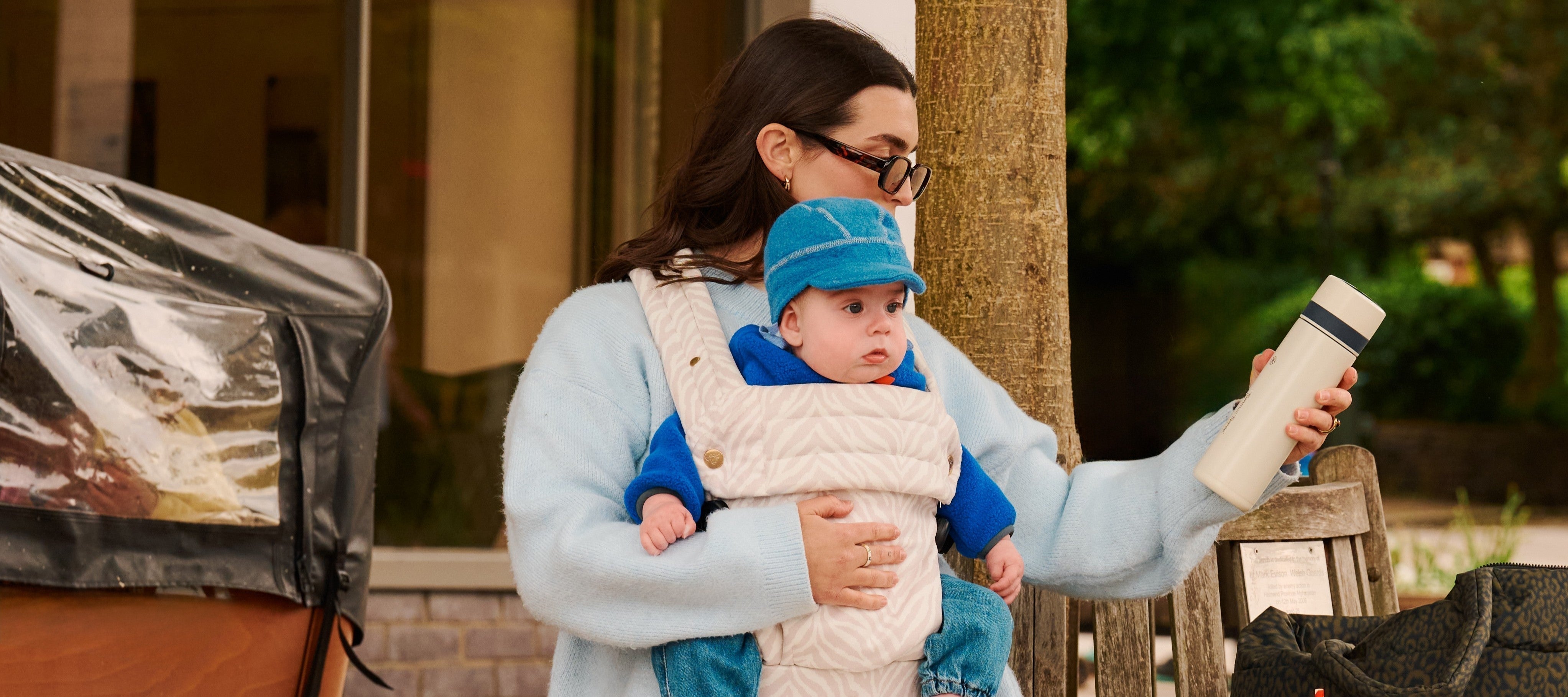 Parent on outdoor bench with baby in wearable carrier holding PrepGo.