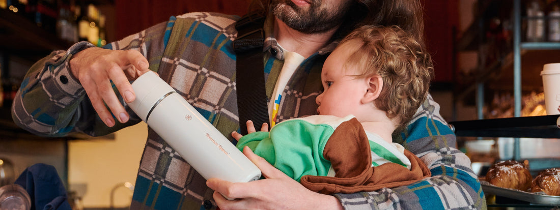 Dad carrying baby against chest while screwing the lid of a PrepGo flask.