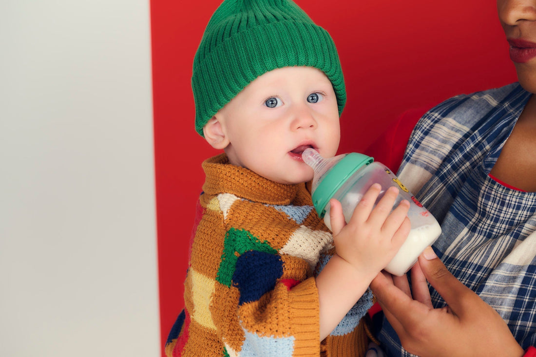 baby wearing green hat holding bottle