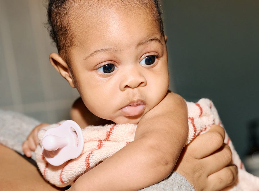 a mum holding her baby who is holding a pink soother