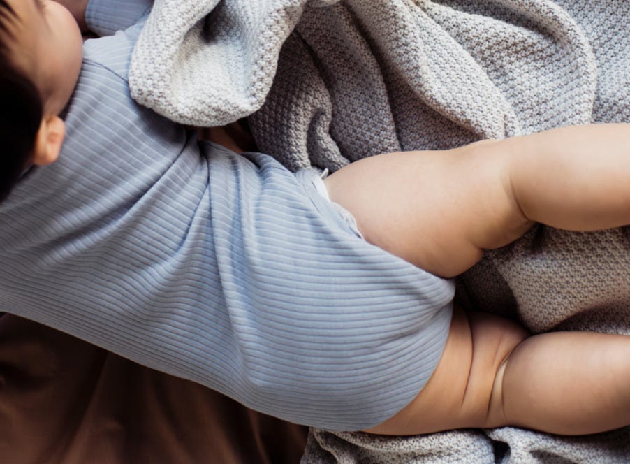 a baby wearing a blue baby grow and a nappy