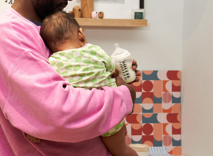 a dad wearing a pink jumper holding his baby