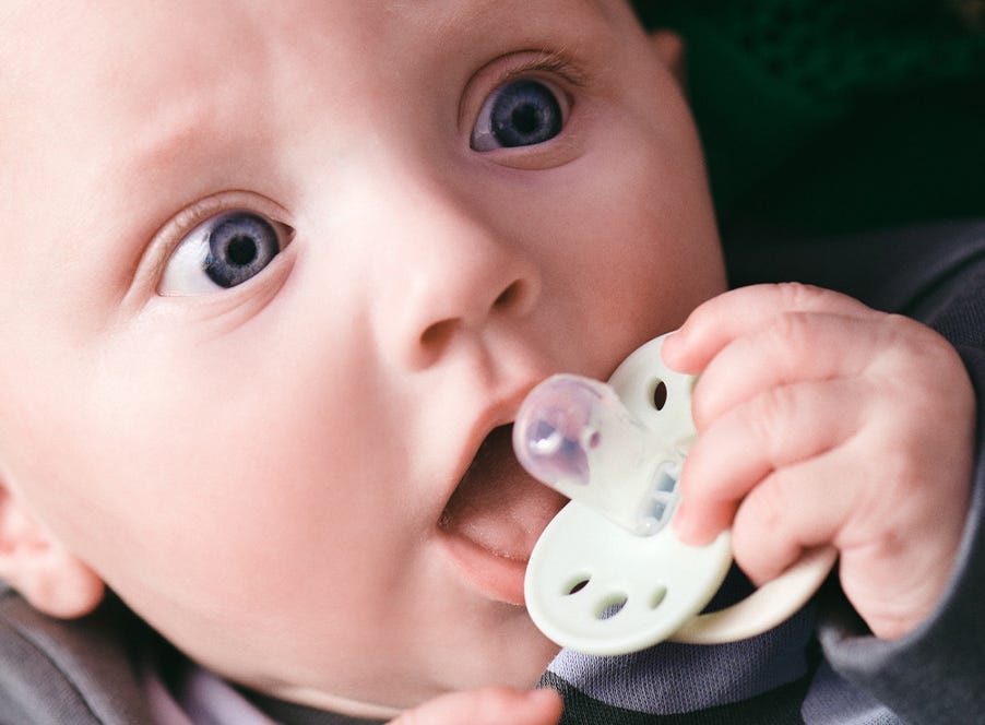 baby holding a pacifier to their mouth