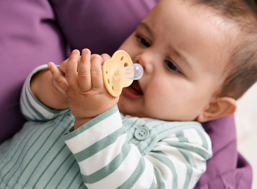 a baby holding a tommee tippee dummmy