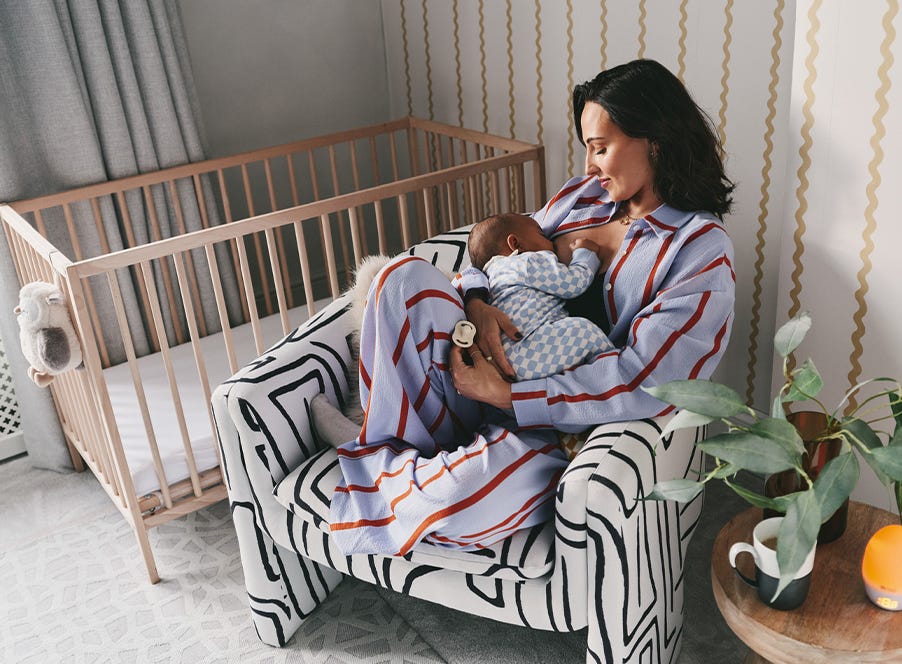 Mum sat on an armchair next to a cot breastfeeding her baby.