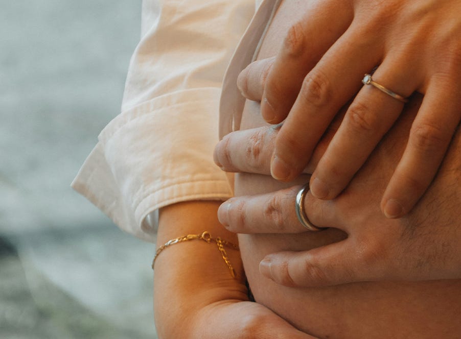 Close-up of a pregnant couple holding hands over the woman's baby bump. 