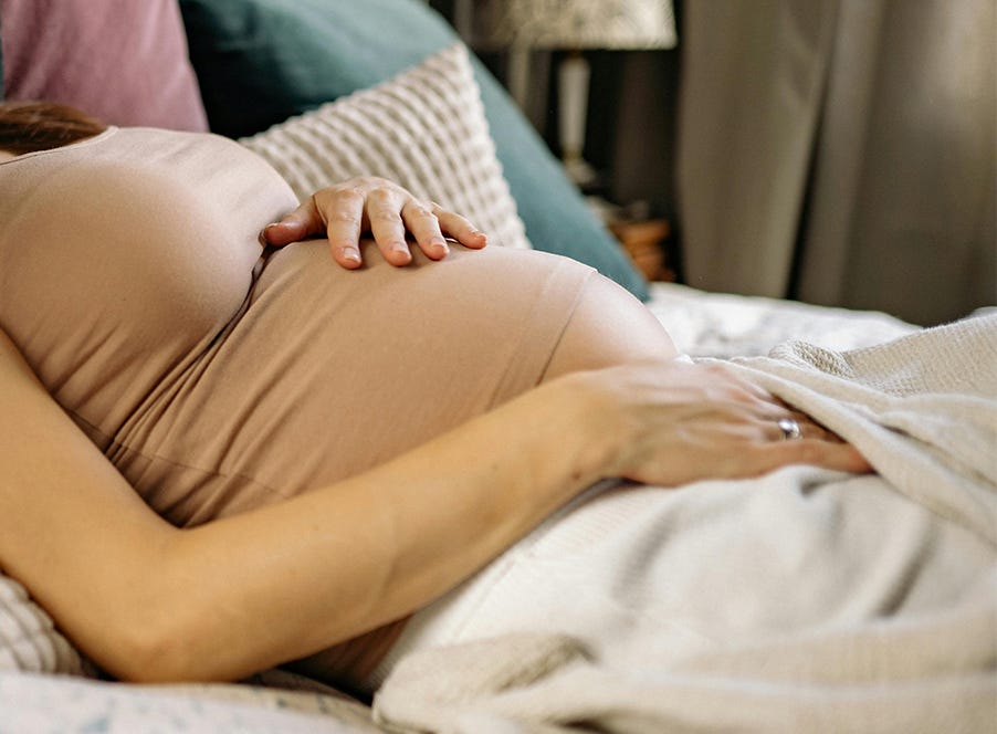 A pregnant woman laying on a bed holding her baby bump.