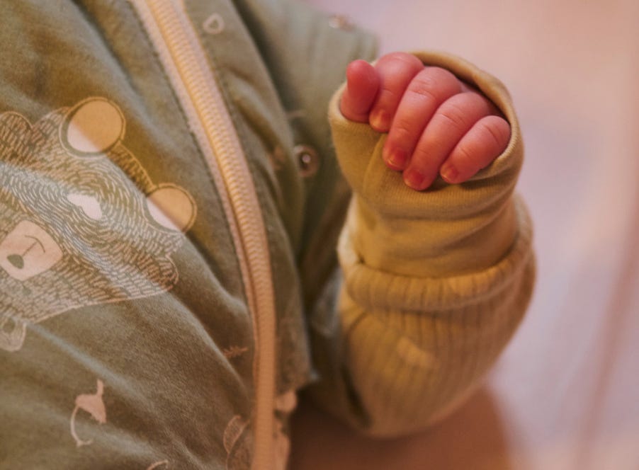 Close up of a baby's hand as they're laying in a crib wearing a sleeping bag
