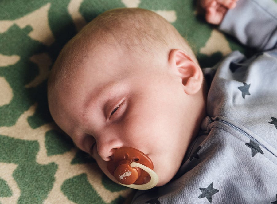 a baby sleeping with a dummy in their mouth