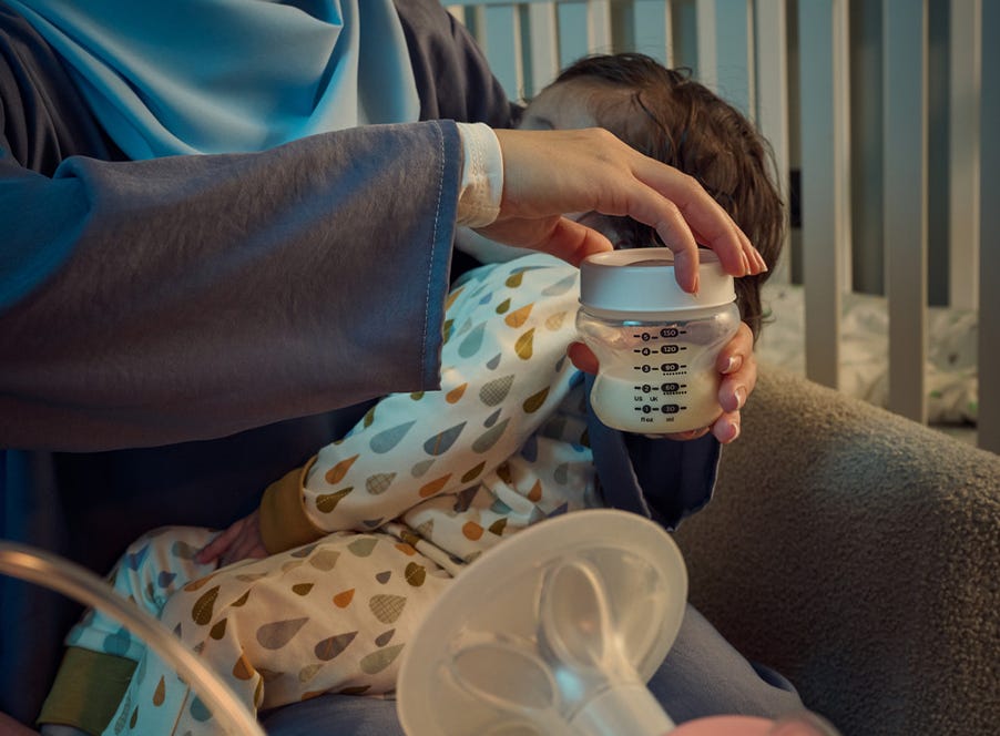 a mum holding her sleeping baby and a tommee tippee bottle