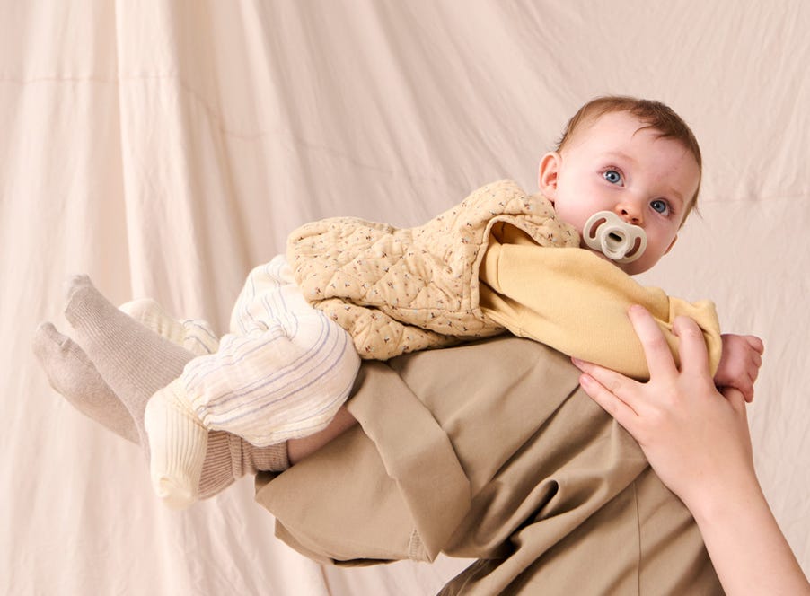 a baby lying on their mums legs, they have a tommee tippee soother in their mouth