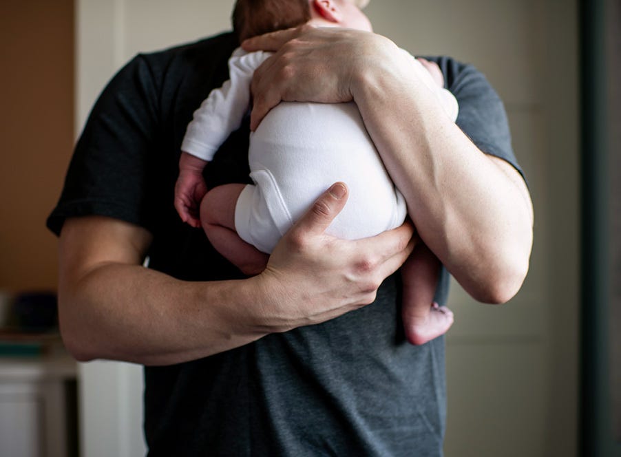 a dad holding his newborn baby who's wearing a white baby grow