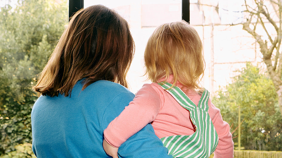 Woman holding a child by a window with trees outside