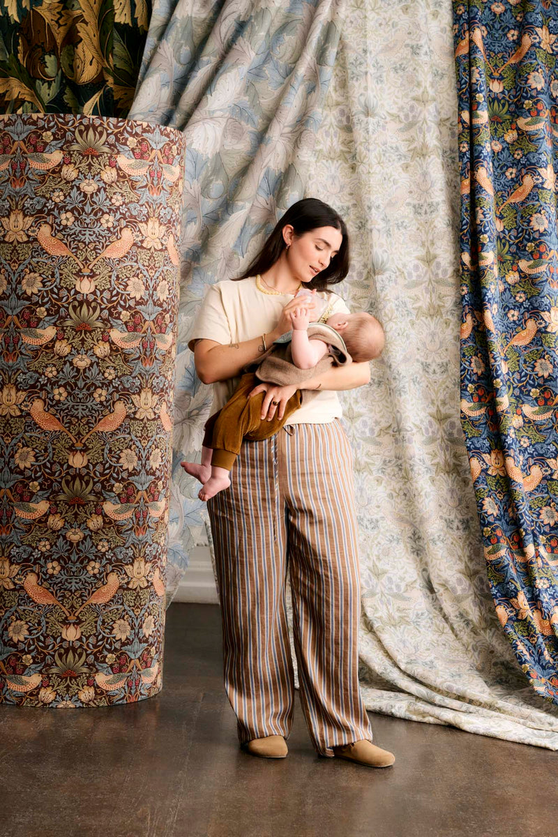 mum feeding baby bottle standing up, surrounded by fabric