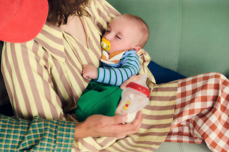 baby asleep on mum with dad holding out the bottle