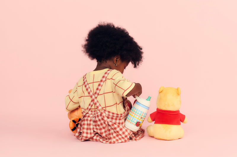 girl sitting with a bottle and winnie the pooh toy