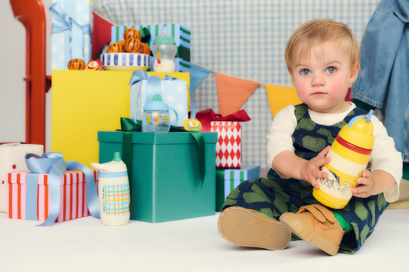 baby holding cup in front of presents and cups