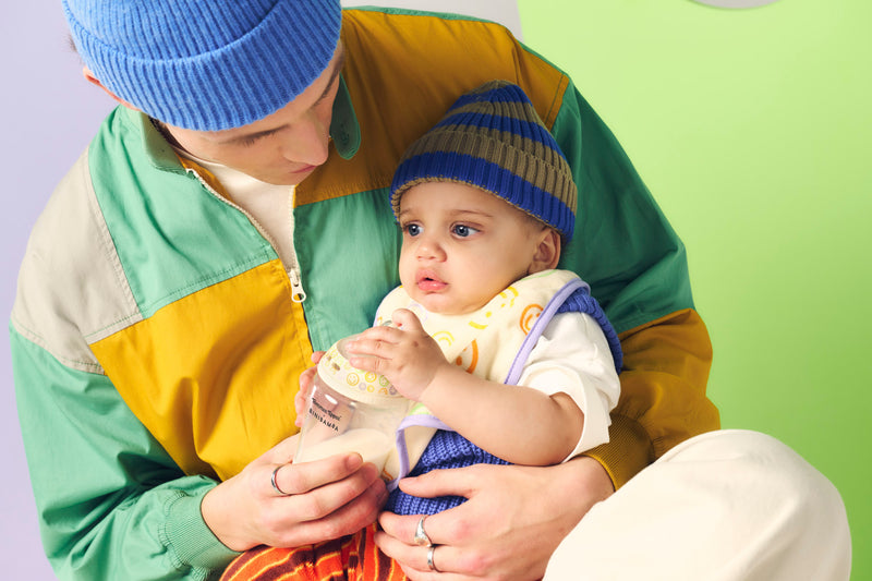 dad holding baby with bottle, wearing hats and bright colours