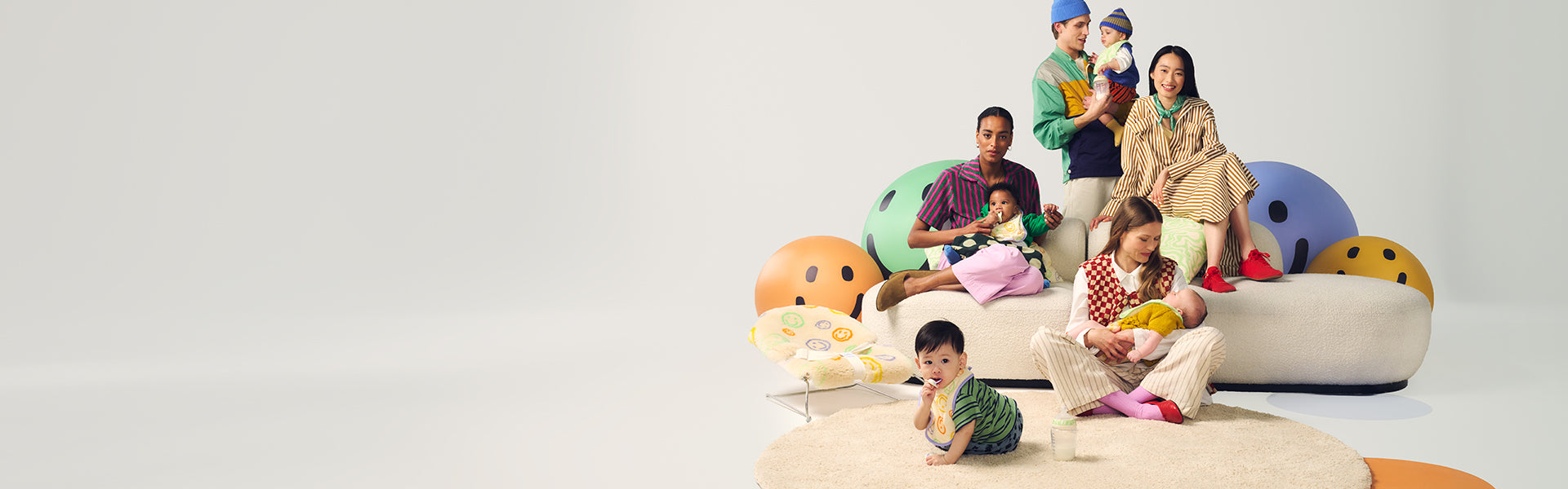 Parents with kids sitting on sofas surrounded by brightly coloured miley faces, showcasing the Tommee Tippee x Binibamba Collection