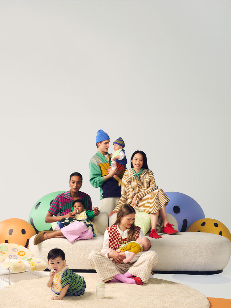 Parents with kids sitting on sofas surrounded by brightly coloured miley faces, showcasing the Tommee Tippee x Binibamba Collection