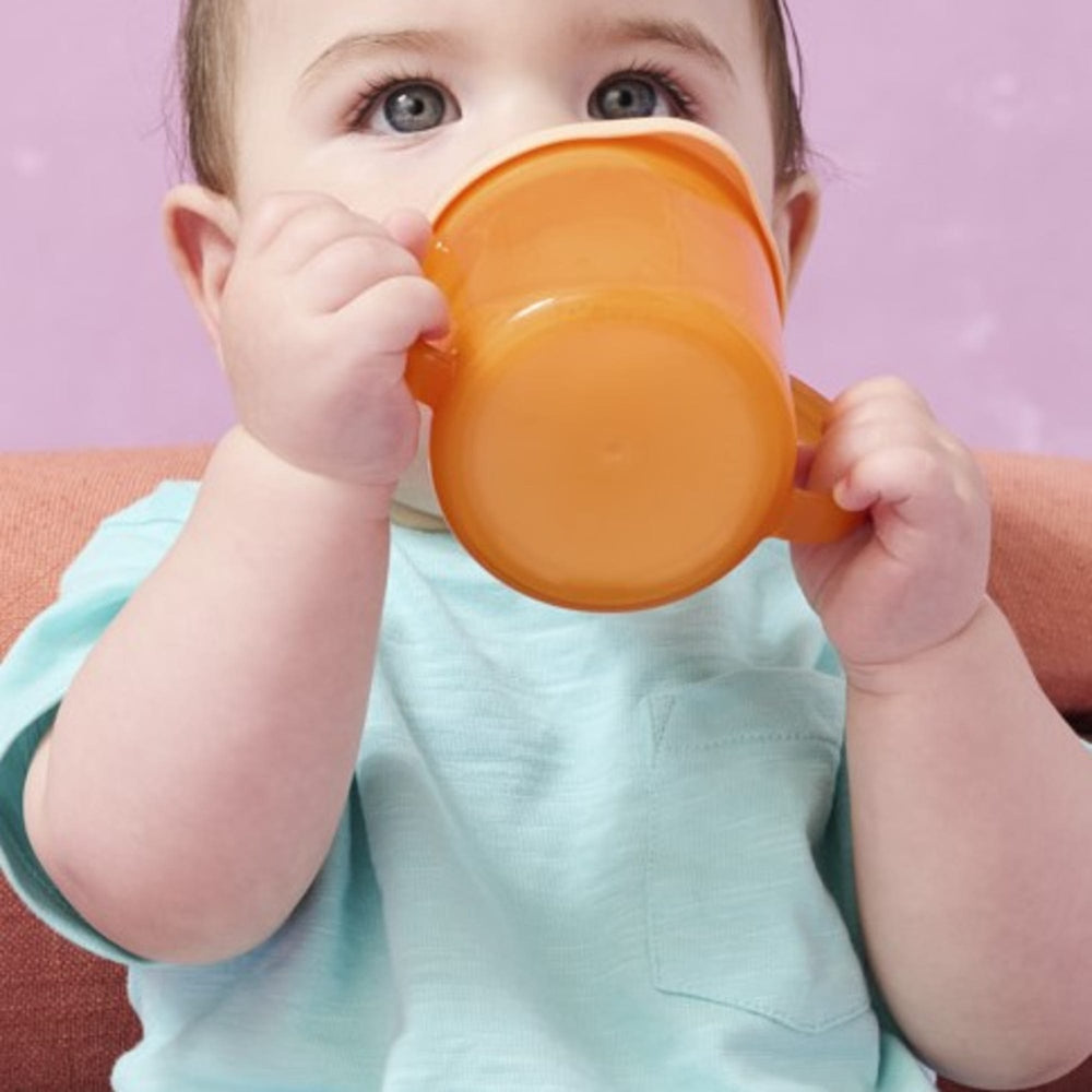 Image of a toddler sat on the floor drinking from an orange first cup