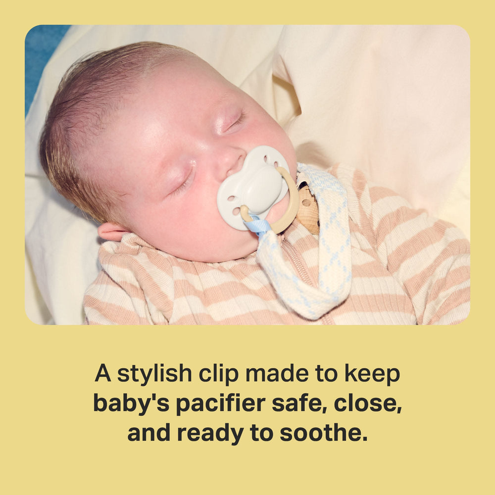 Parent holding baby with pacifier clip attached to clothing with feature text.