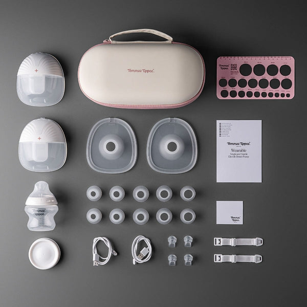 Flat lay shot on a charcoal background showing: assembled motor and milk collectors carry case measurement guide horns baby bottles storage lid inserts bra strap adjusters.