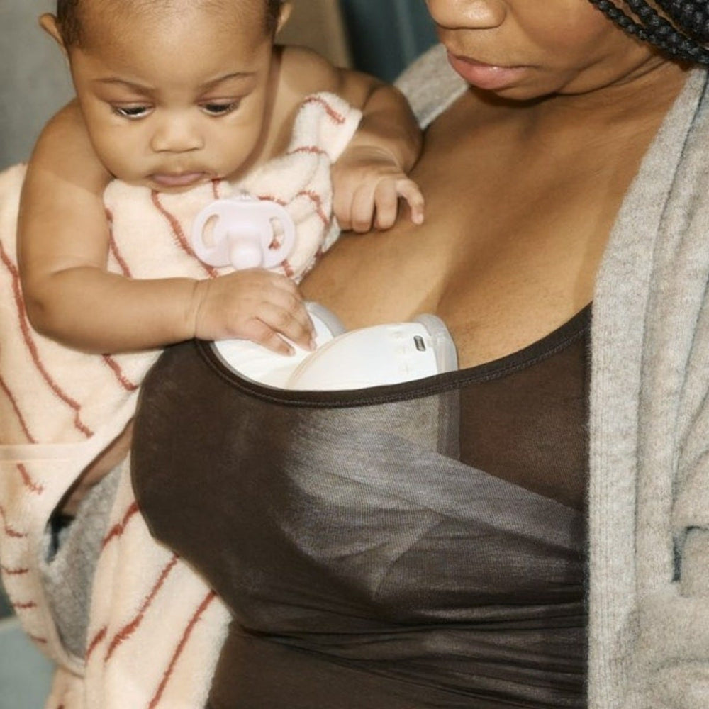 Parent expressing with two in-bra wearable breast pumps while holding baby with an Ultra-light soother.