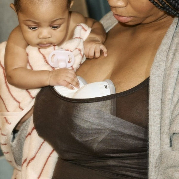 Parent expressing with two in-bra wearable breast pumps while holding baby with an Ultra-light soother.
