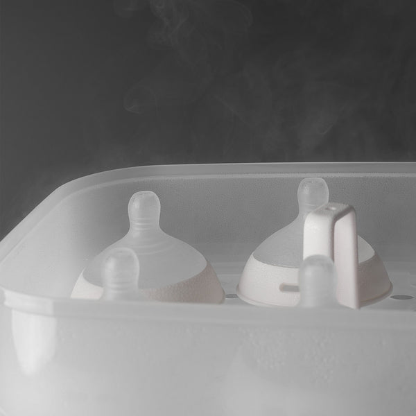 Open SteriDryer with steam coming out of it and showing bottle lids inside against a grey background