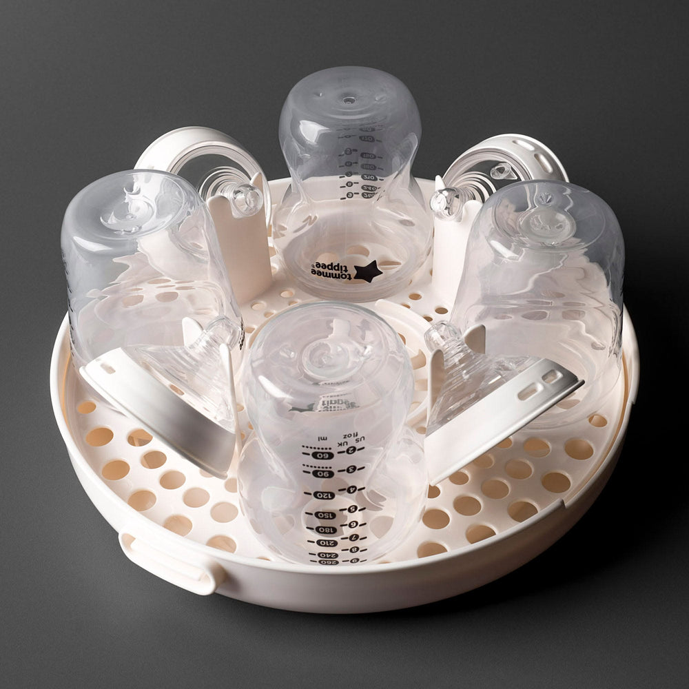 Microwave sterilizer open and filled with bottles against a dark grey background