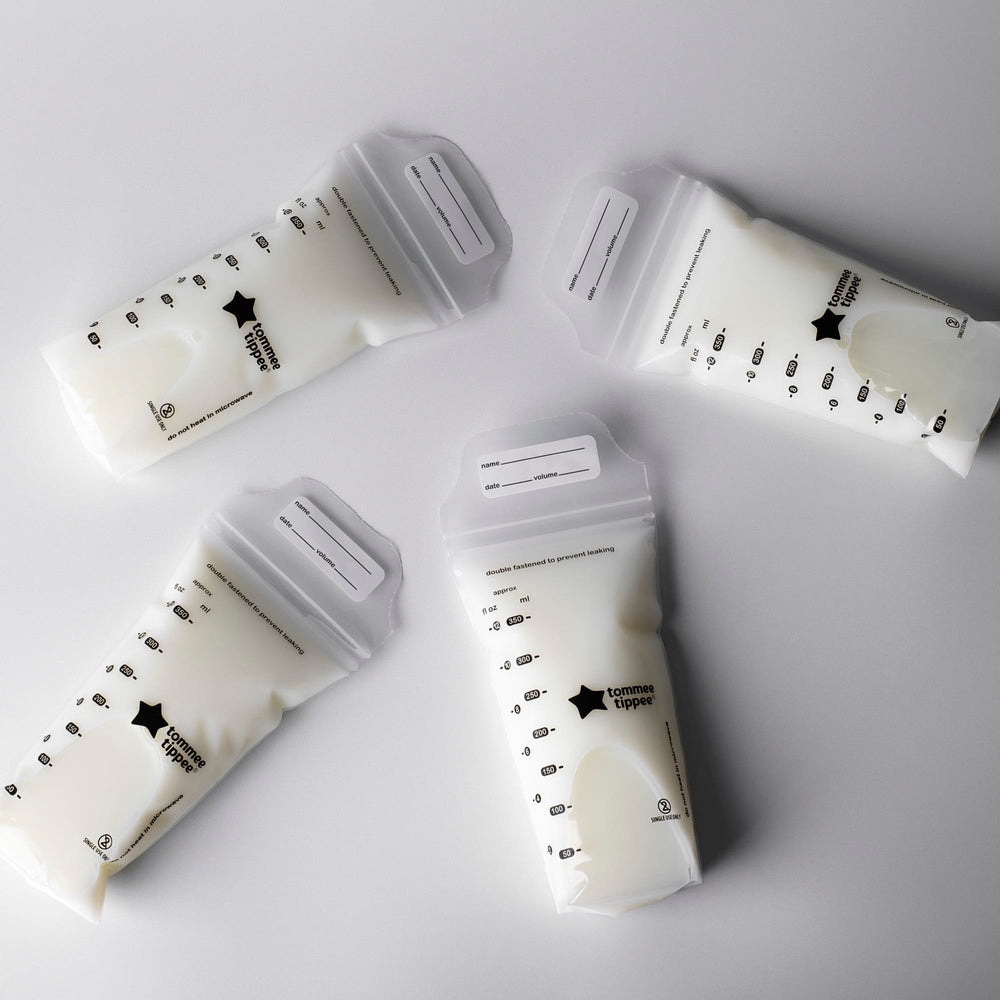 Five filled breast milk storage bags laying on a light grey background.