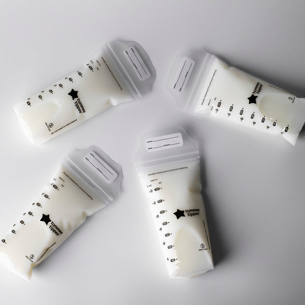 Five filled breast milk storage bags laying on a light grey background.
