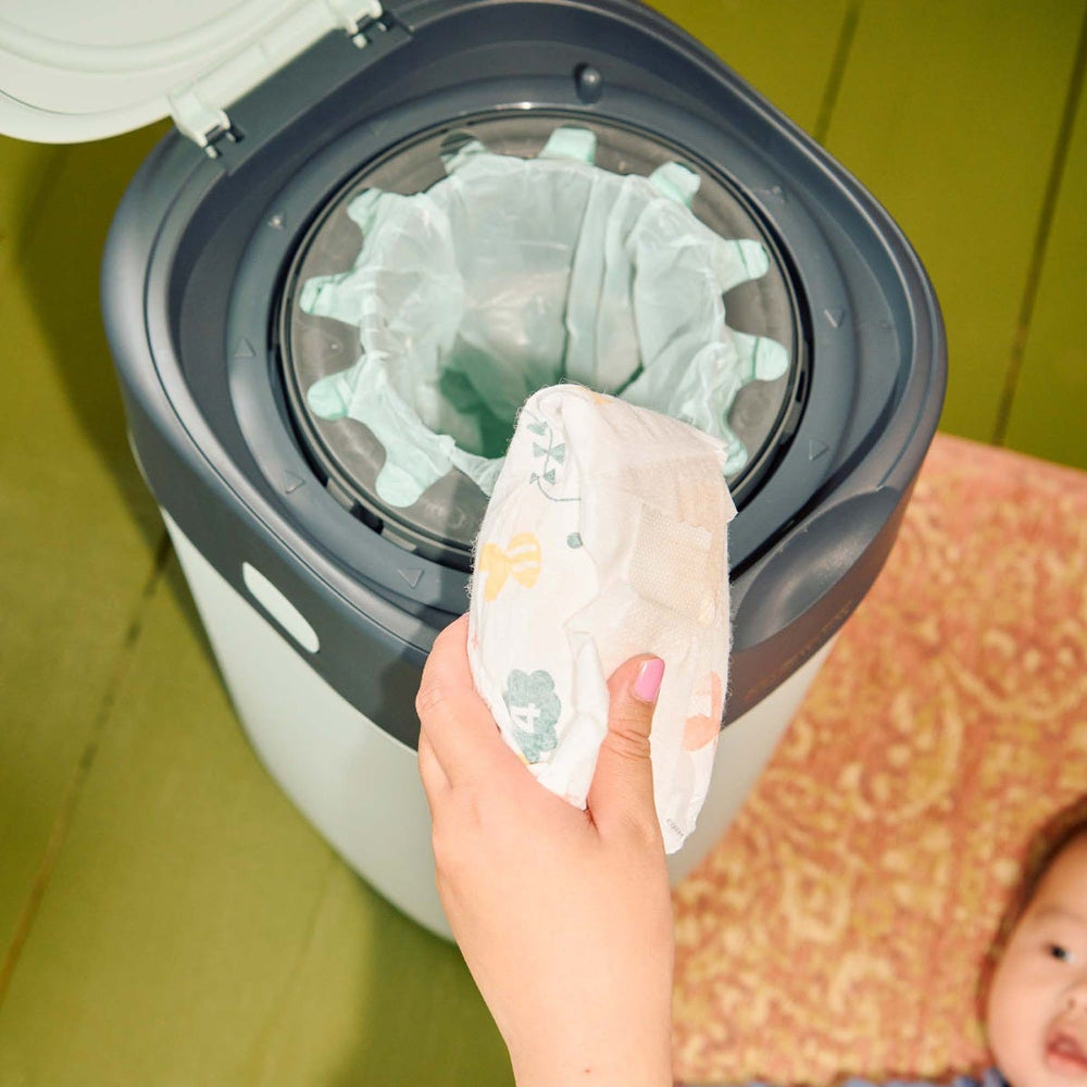 Image d'un parent qui met une couche dans une poubelle verte twist and click