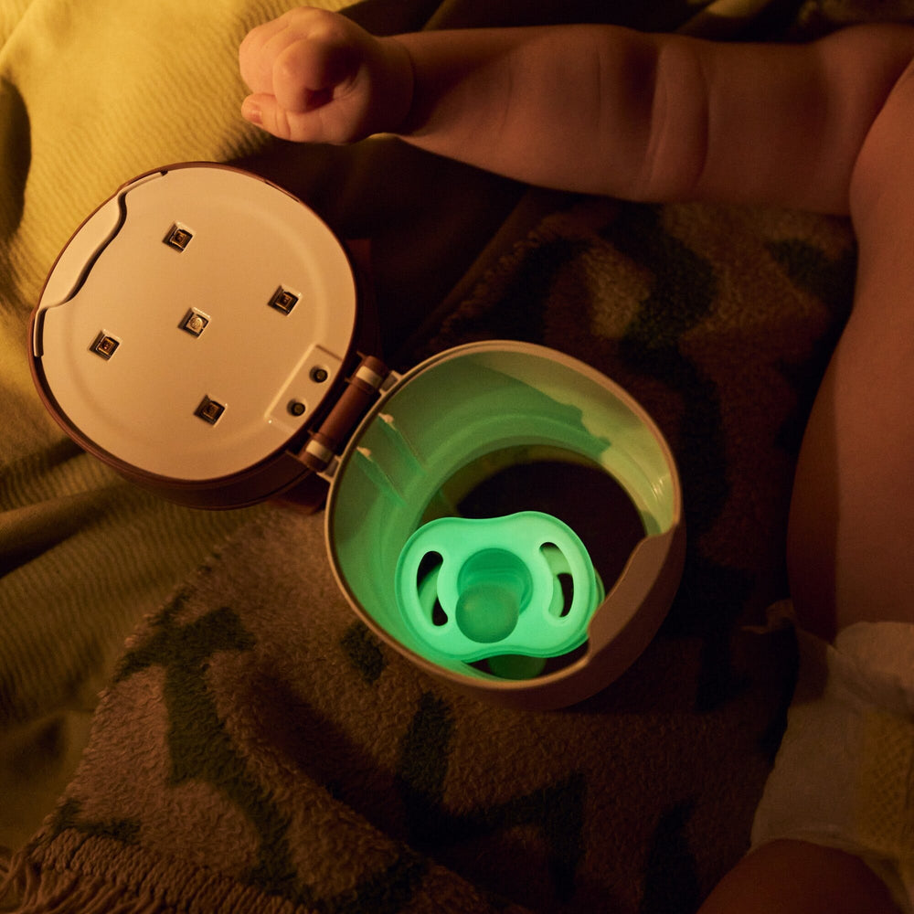 Baby laying next to a charged Ultra-light NightGlow soother inside the NightGlow Pod.