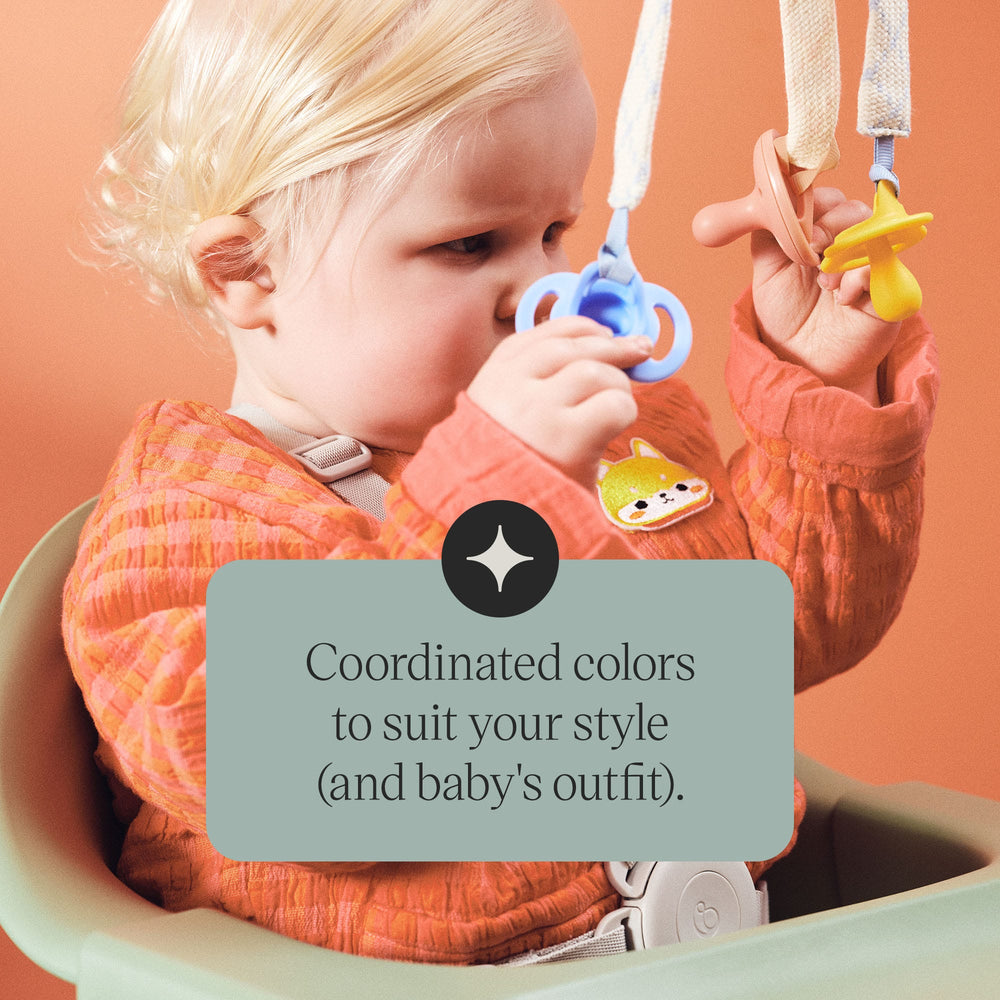 Baby holding pacifiers attached to comforter clips with text about the style.