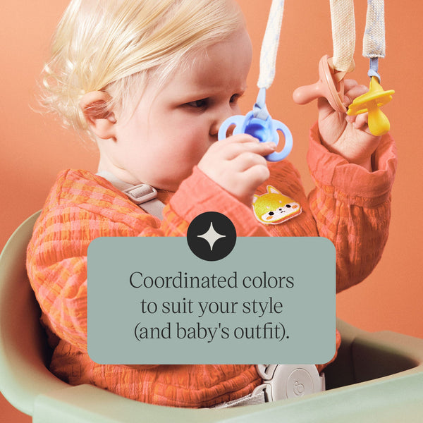 Baby holding pacifiers attached to comforter clips with text about the style.