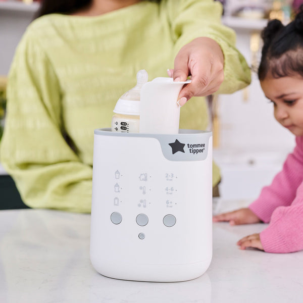 A woman using the easy-lift cradle to lower a baby bottle into a Multiwarm bottle warmer