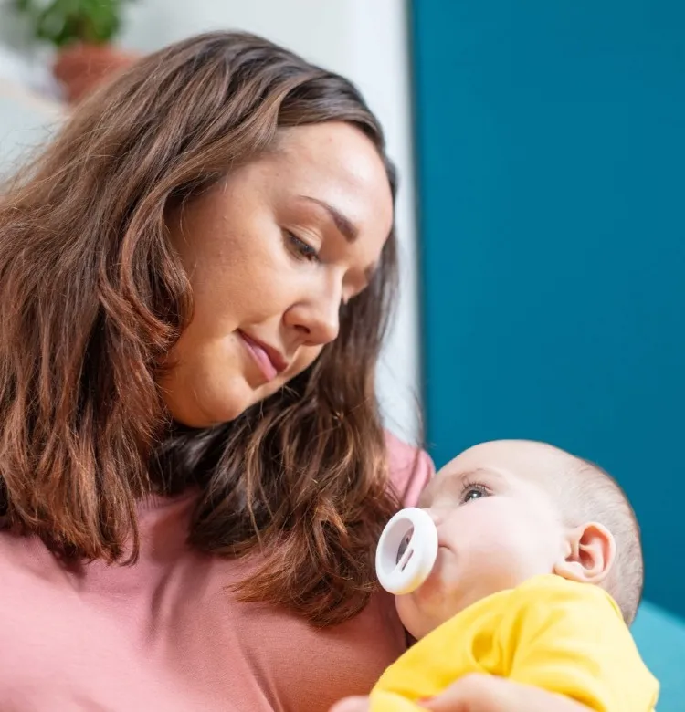 Symptoms and Support for Postnatal Depression Mom holding her baby who has a Tommee Tippee pacifier in their mouth