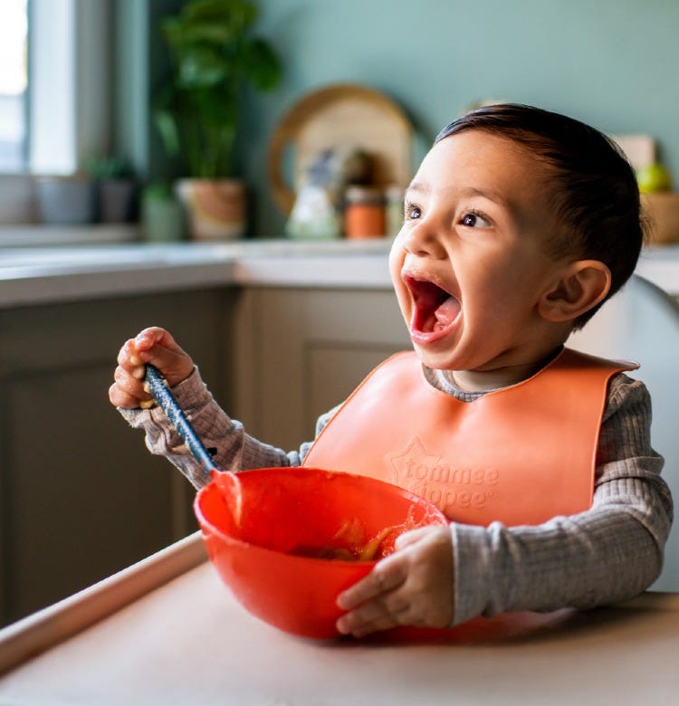 How to Wean Off Breastfeeding and Bottle Feeding Baby sitting in their high chair wearing an orange bib and eating from an orange bowl
